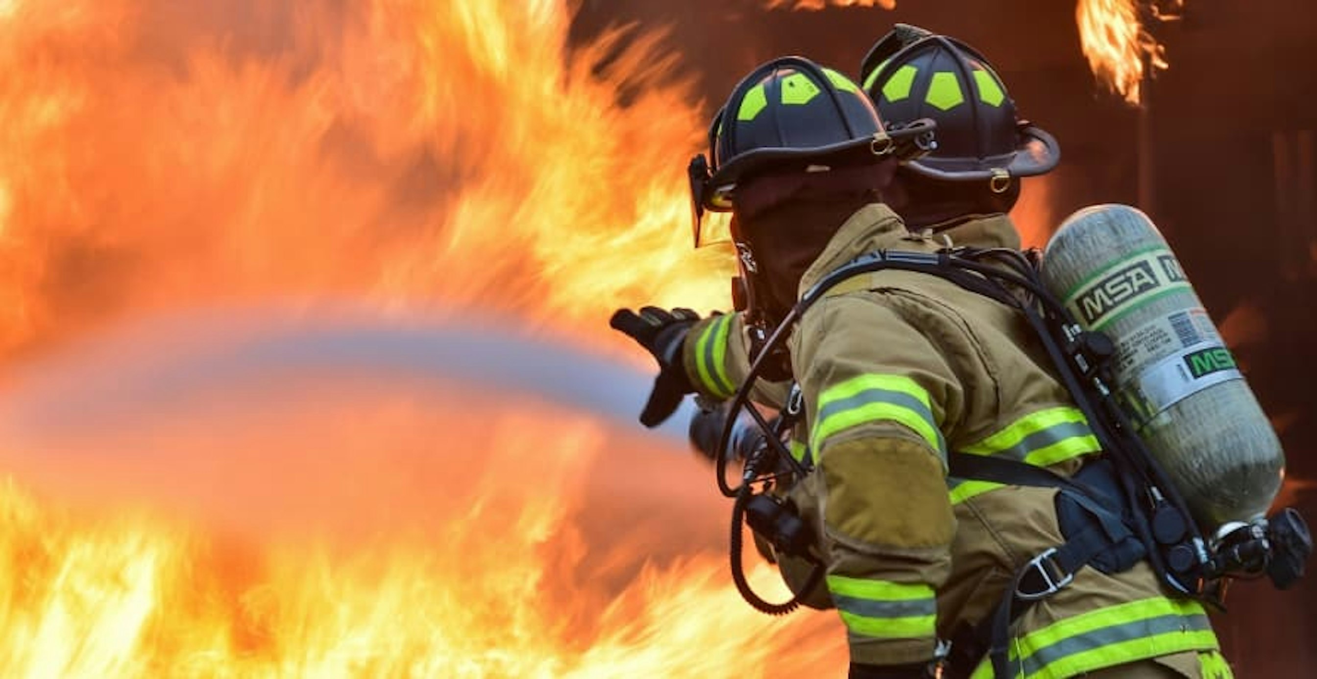 two firefighters pouring water onto large fire