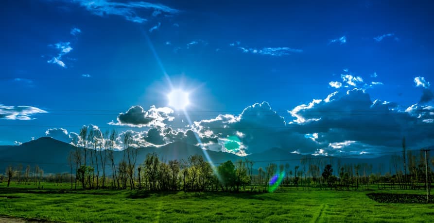 blue sun shining sky with green grass and mountains