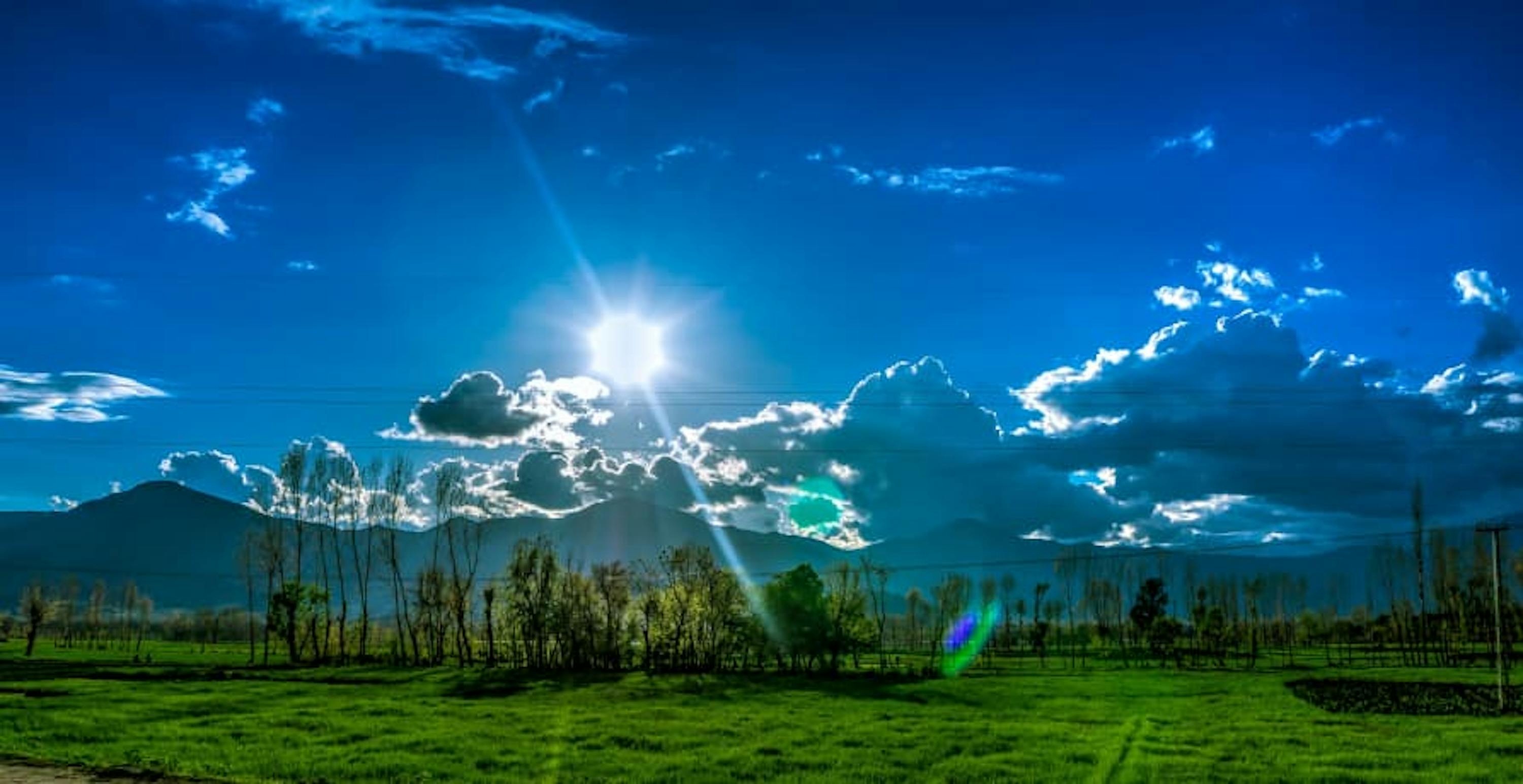 blue sun shining sky with green grass and mountains