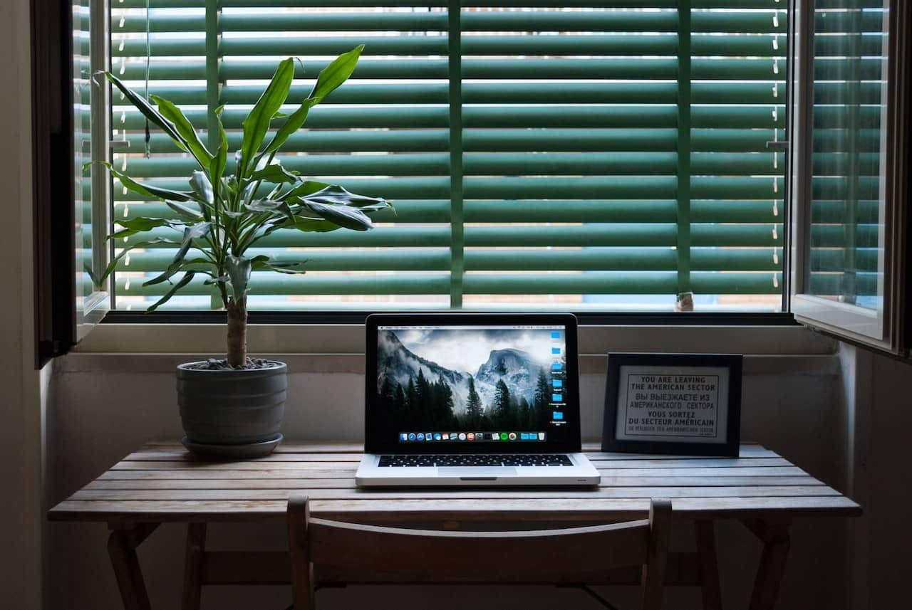 Macbook Air sur une table à côté d'une plante d'intérieur et d'un cadre photo.