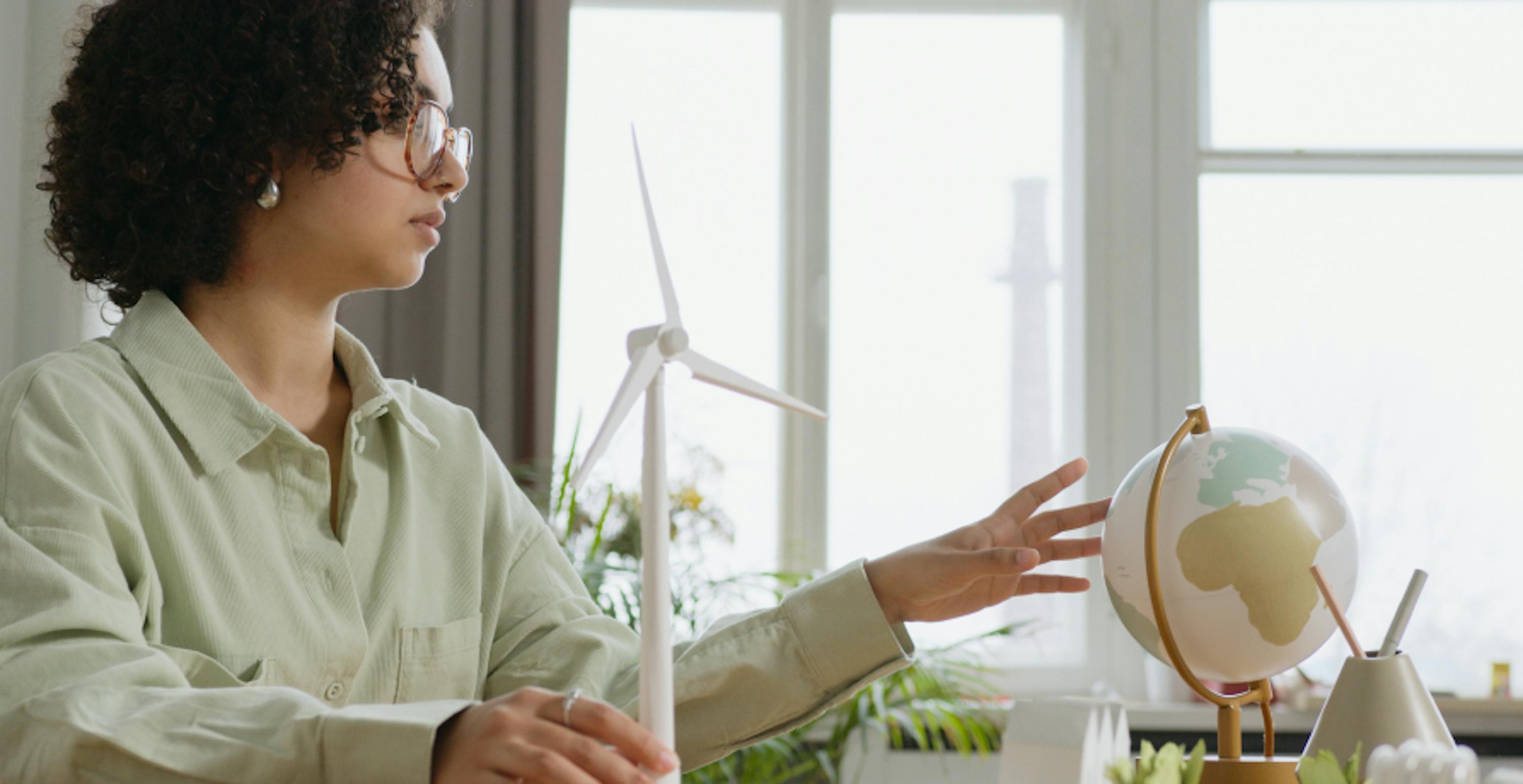 une femme avec une éolienne de petite taille et une mappemonde devant elle