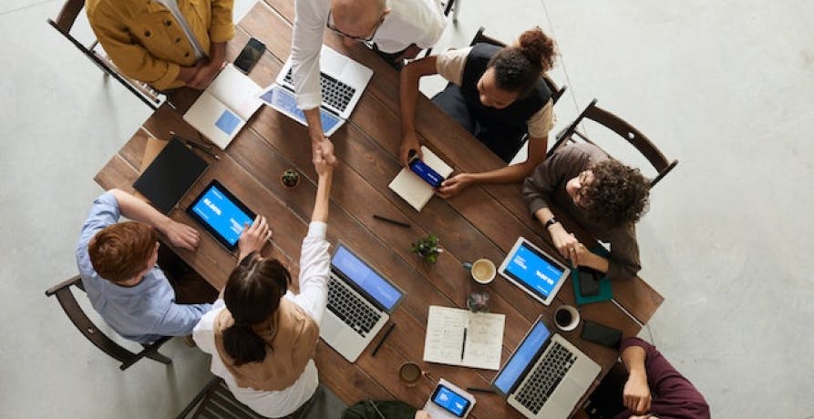 people huddled around wood meeting table with laptops bird's eye view