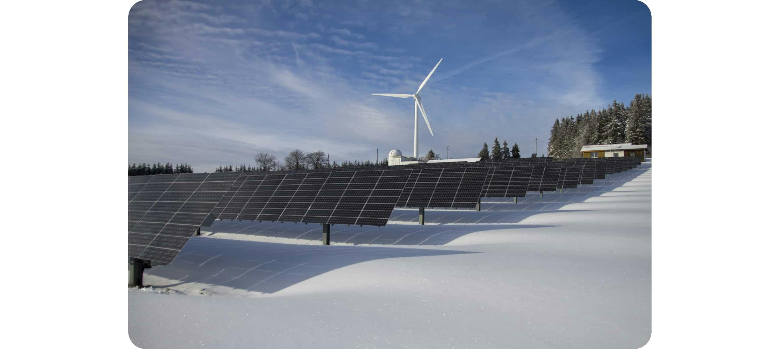 Solar panels on snow with windmill under clear day sky