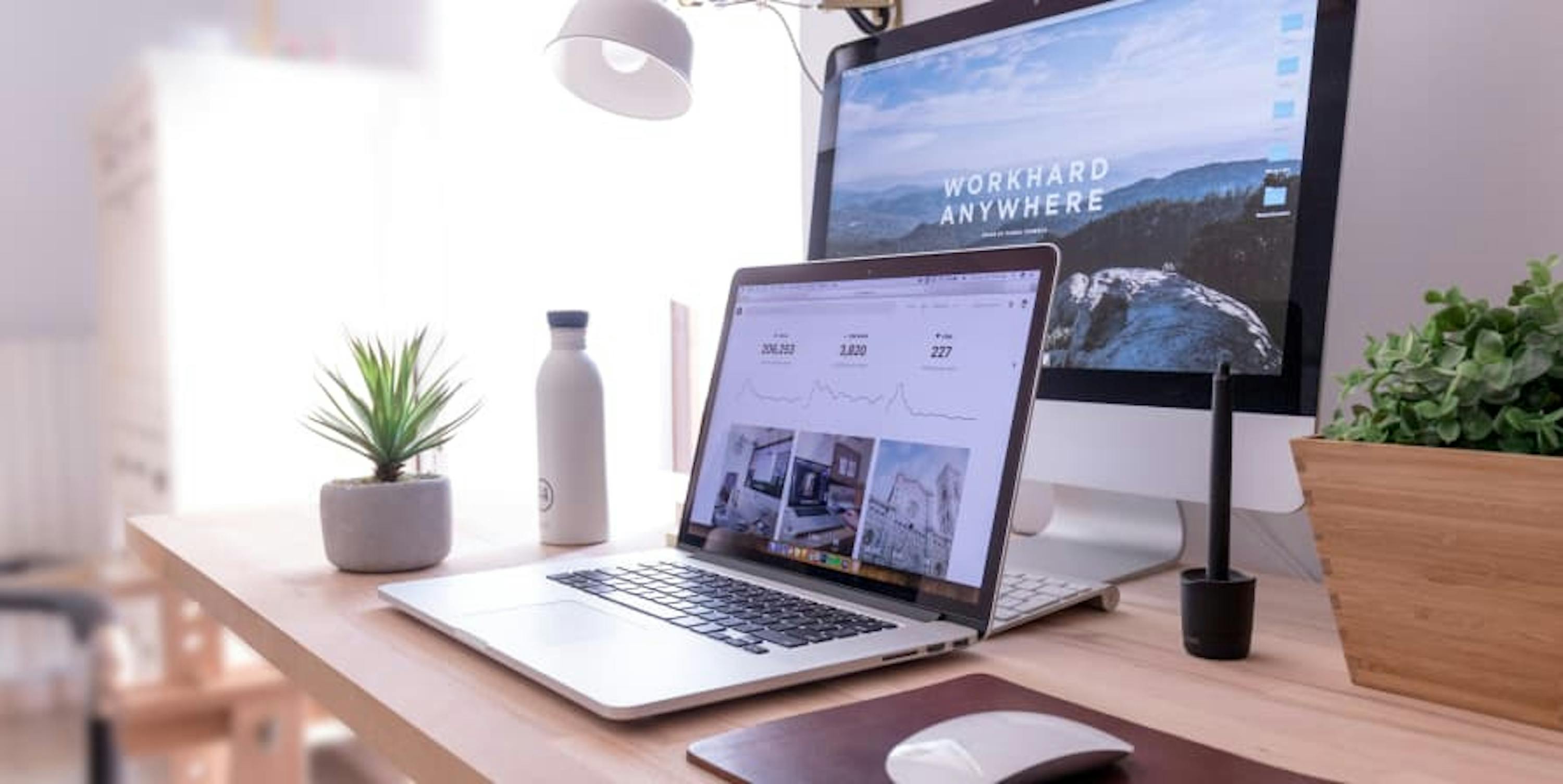 laptop and desktop on wood desk with green plants