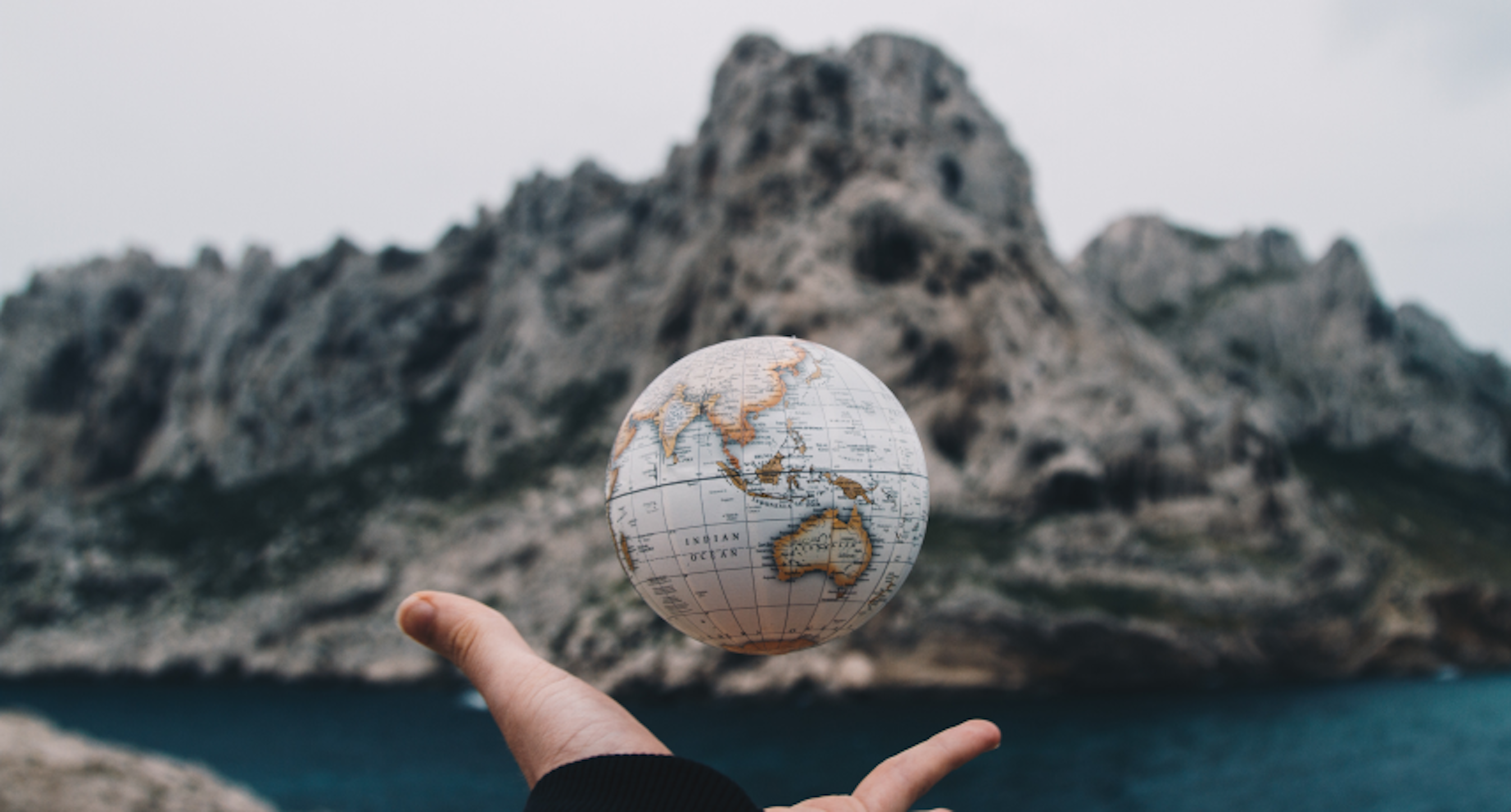 person tossing mini globe in front of lake and rocks