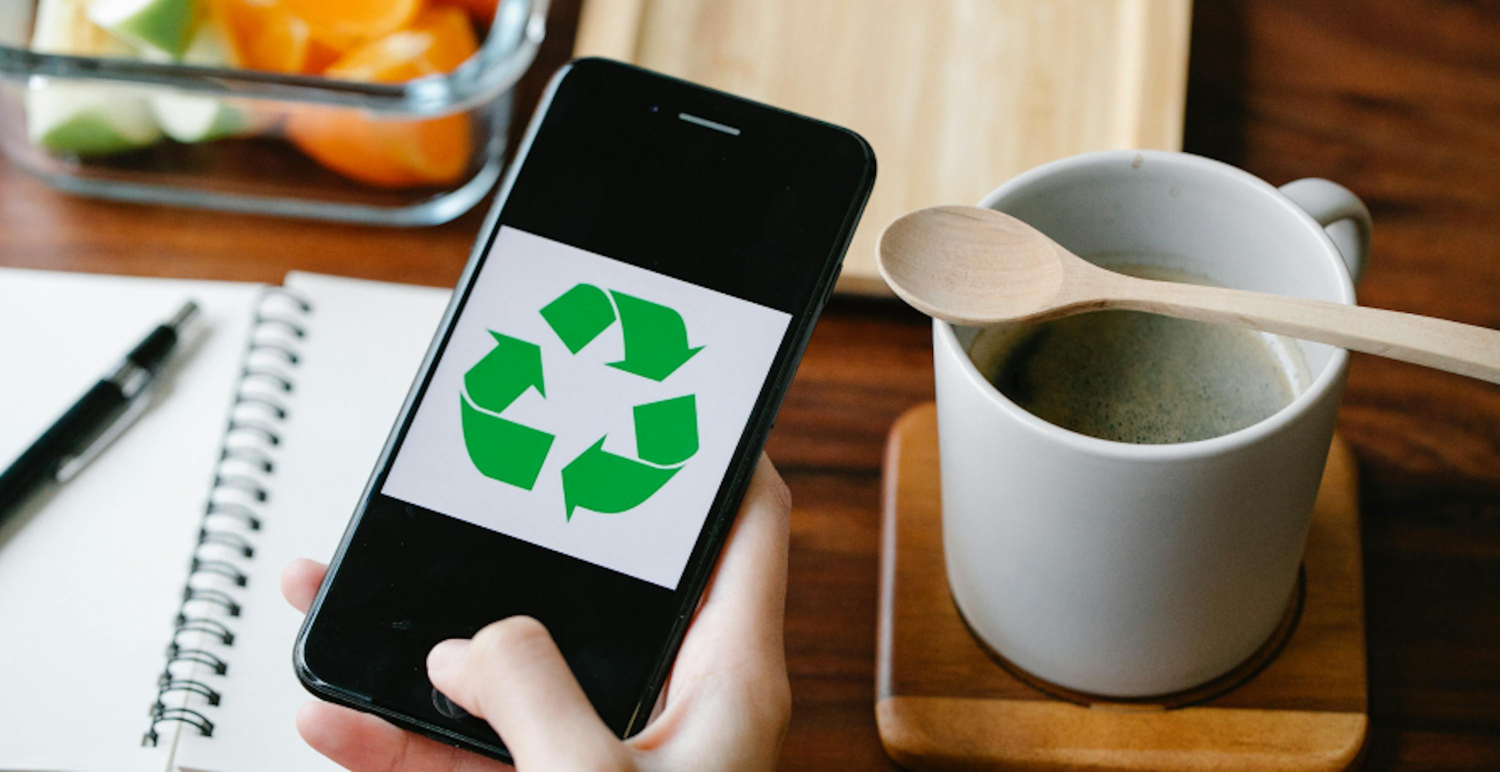 phone with recyccling symboal against minimalistc mataha mug, notebook, and fruits in glass tubberware