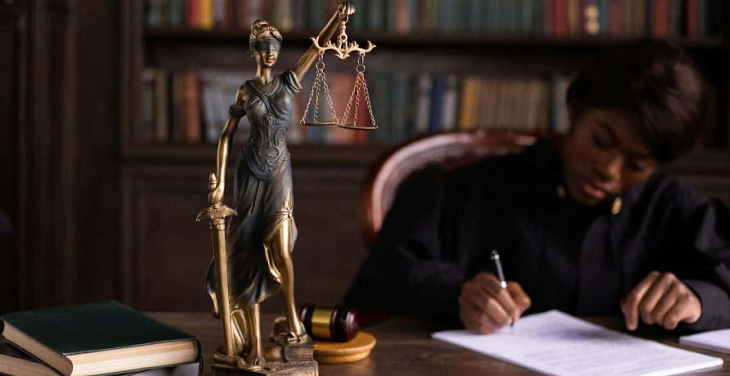 a female judge in a legal library with a statue of lady justice in front of her