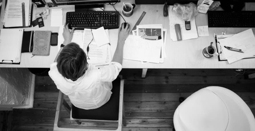 man sitting at a work desk on his computer with reports and documents around him