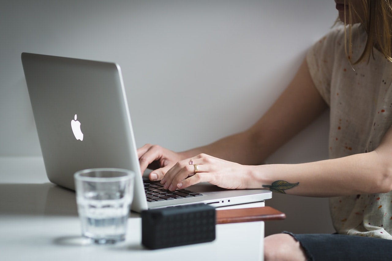 Une femme utilisant un Macbook près d'un verre sur une table