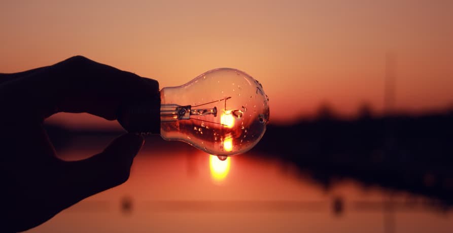 someone holding a wet lightbulb in front of a sunset