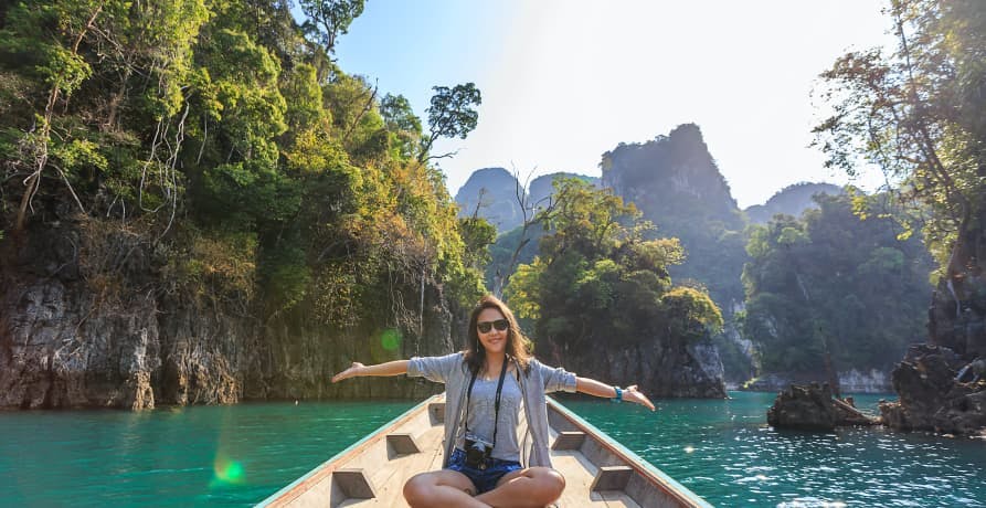 woman with her arms out, sitting on a boat in a beautiful tropical lagoon with lots of palm trees