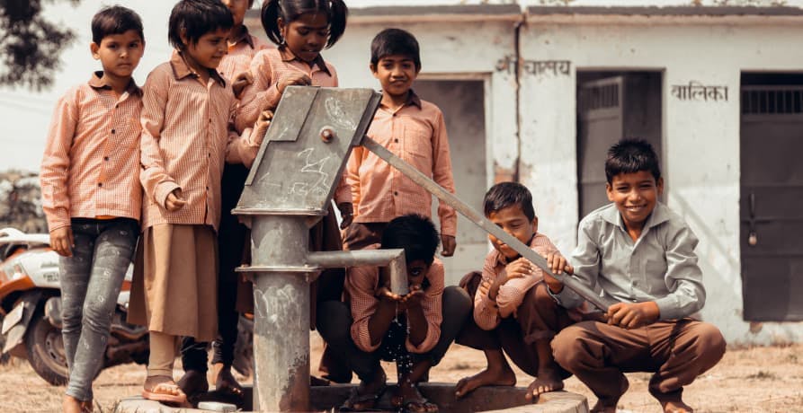 children in India standing in front of a water fountain