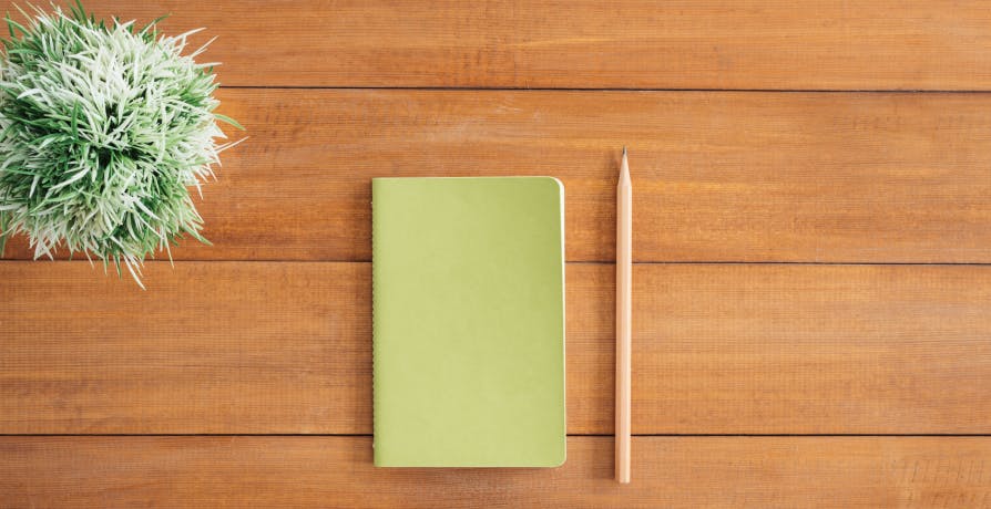 green notebook with wooden pencil on table with plant