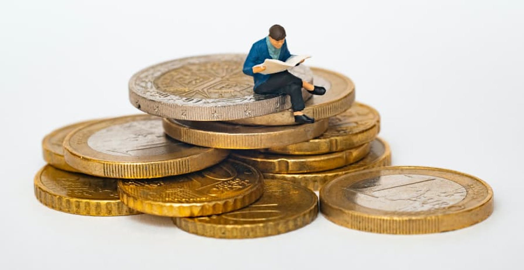 person reading book sitting on top of euro coins
