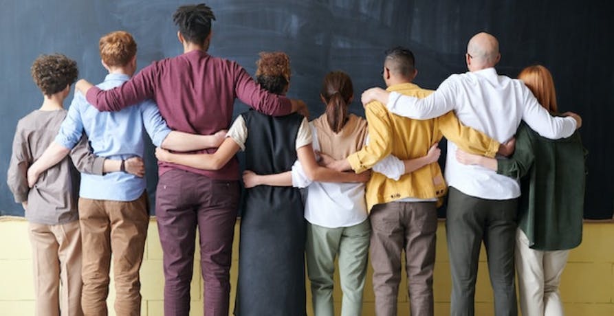 employees of different colors arms around each standing in front of a blackboard
