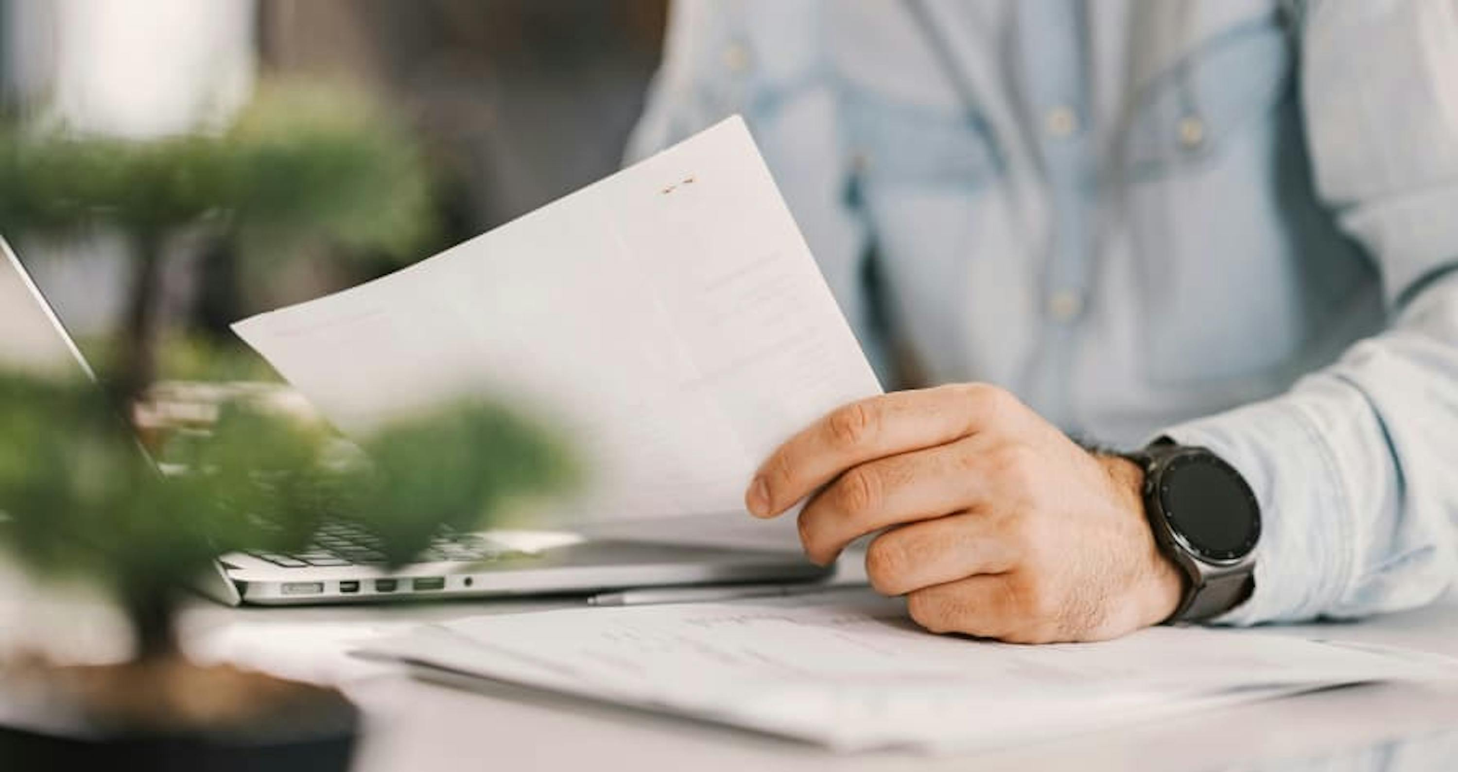 person holding paper at desk with plant