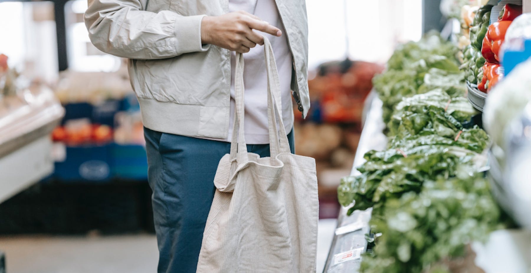 un homme devant le rayonsdes légumes portant un tote bag