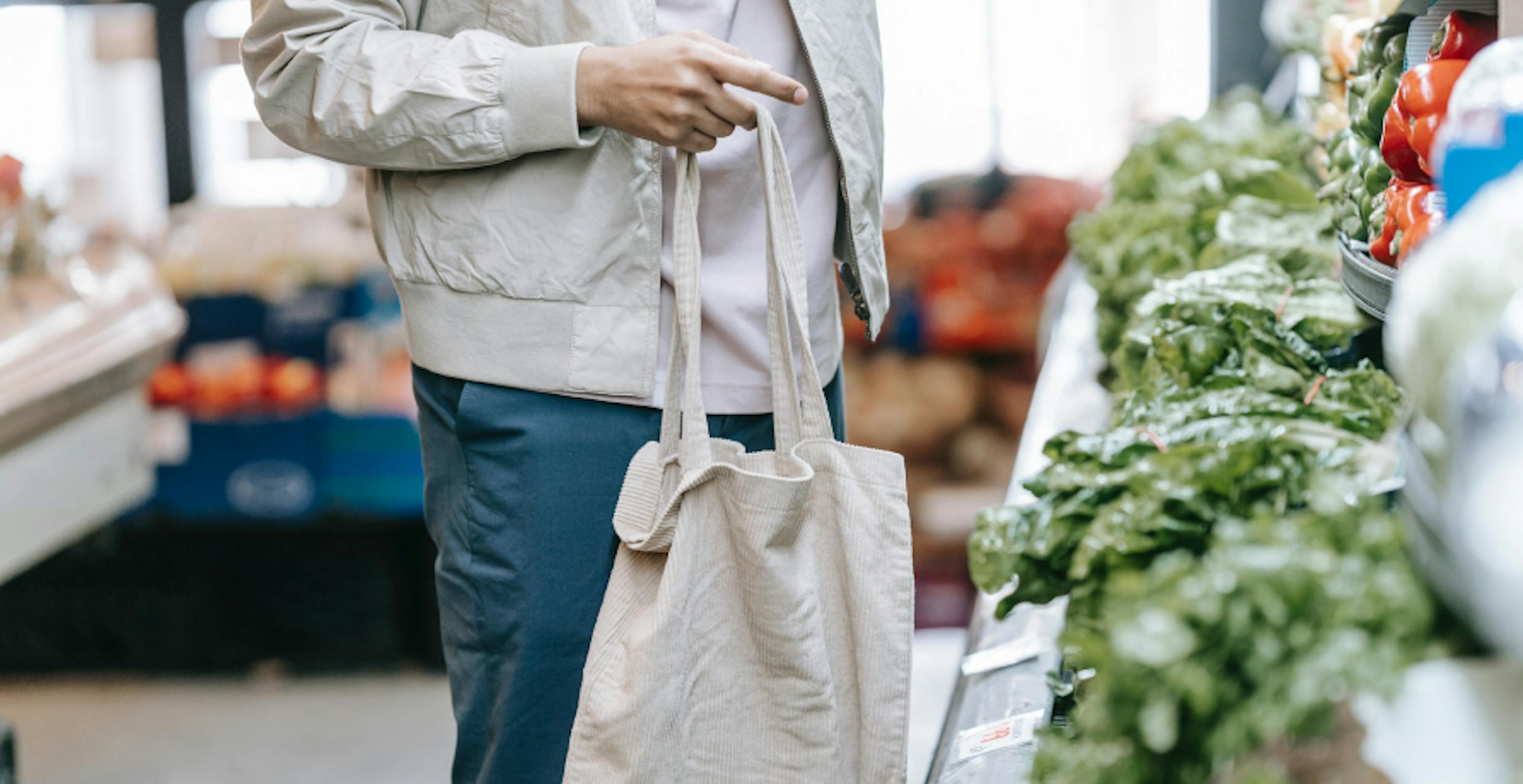 un homme devant le rayonsdes légumes portant un tote bag