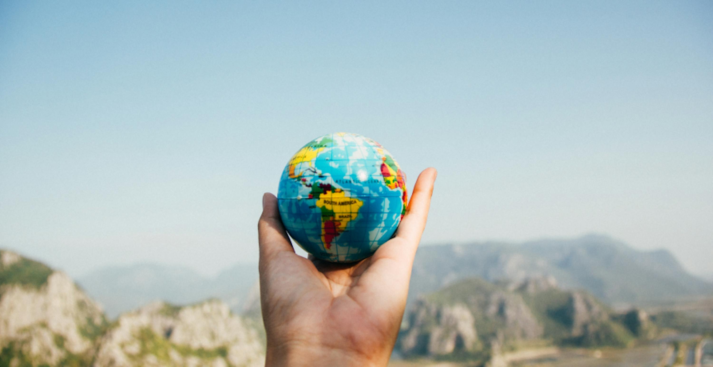 person holding a small globe in natural landscape