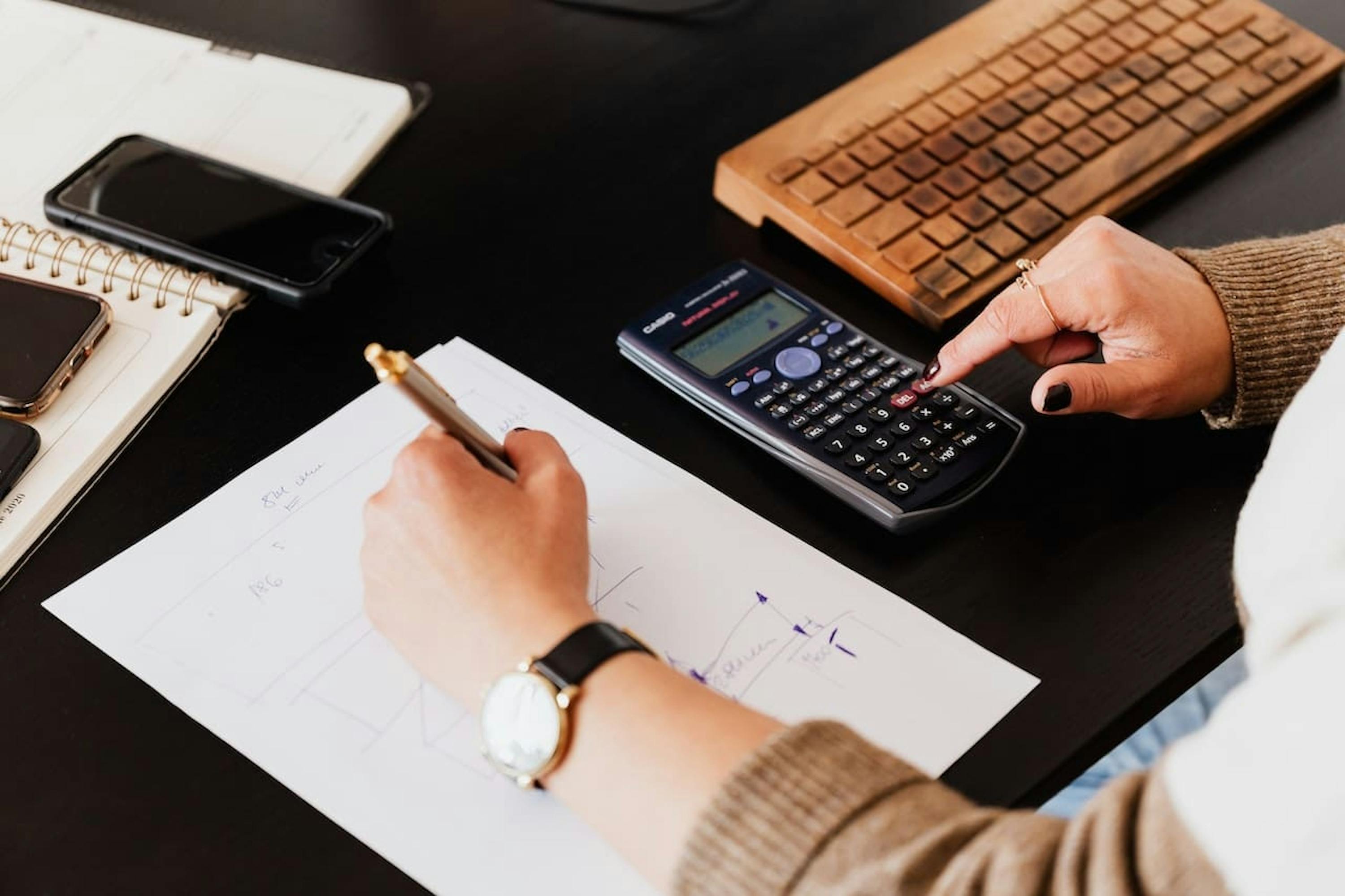 une personne écrivant sur du papier tout en utilisant une calculatrice