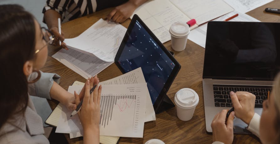 people in a meeting with coffee, papers, and laptops
