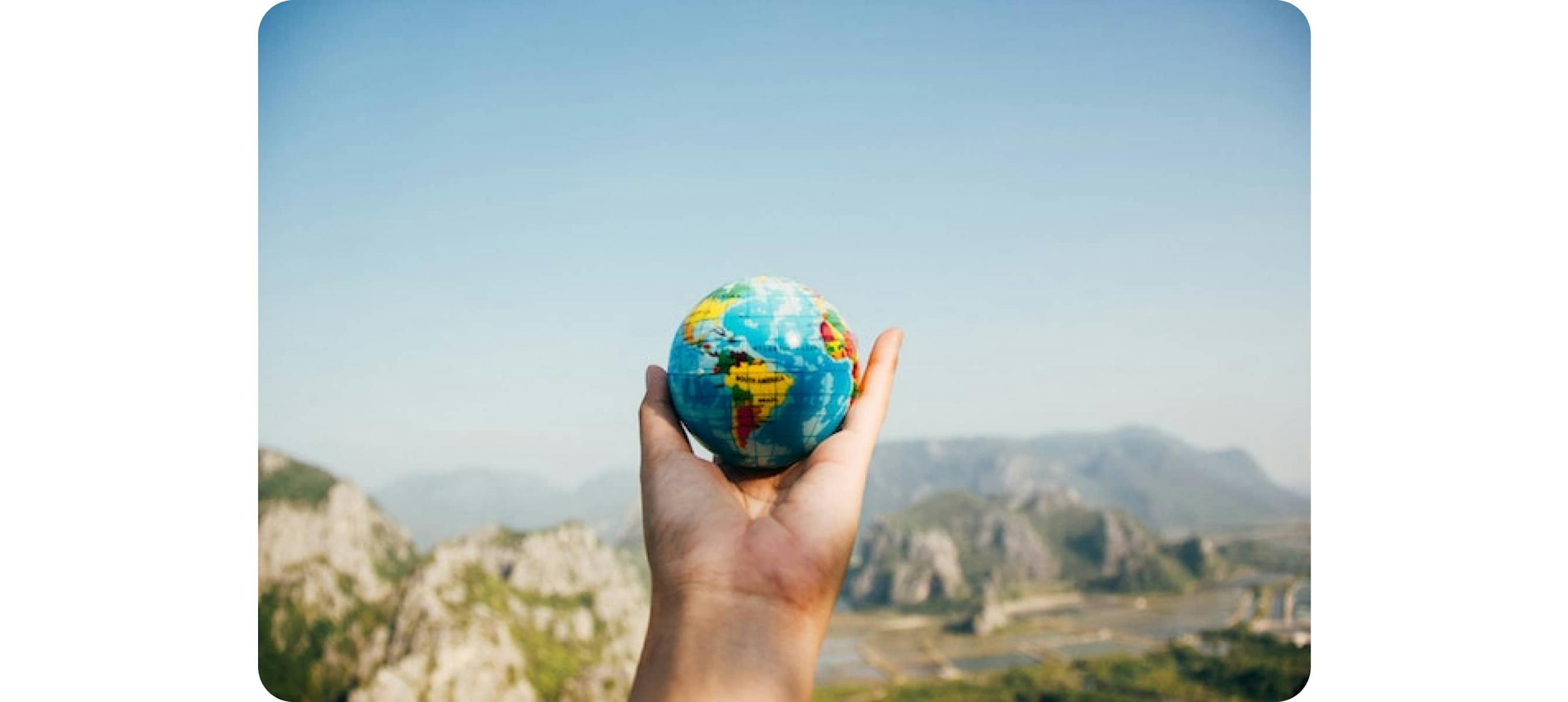 Person holding the globe in front of the mountain