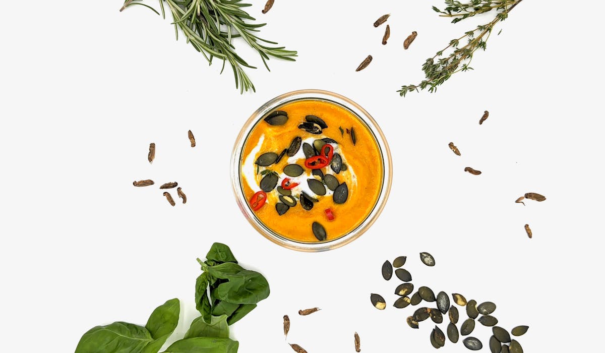 Top view of pumpkin soup in a bowl decorated with seeds and chili