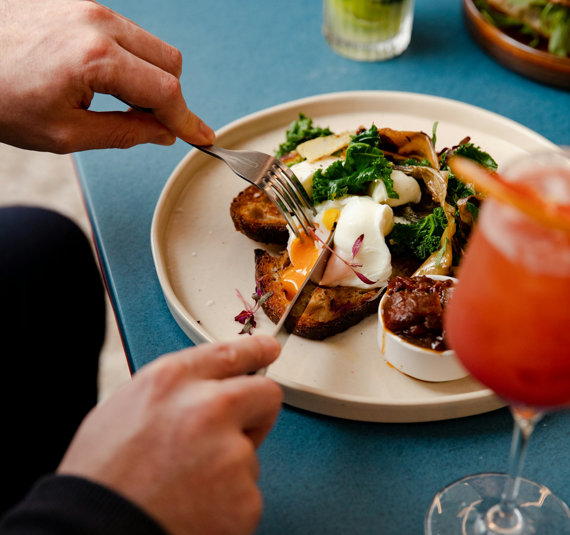 person cutting open poached egg with knife and fork