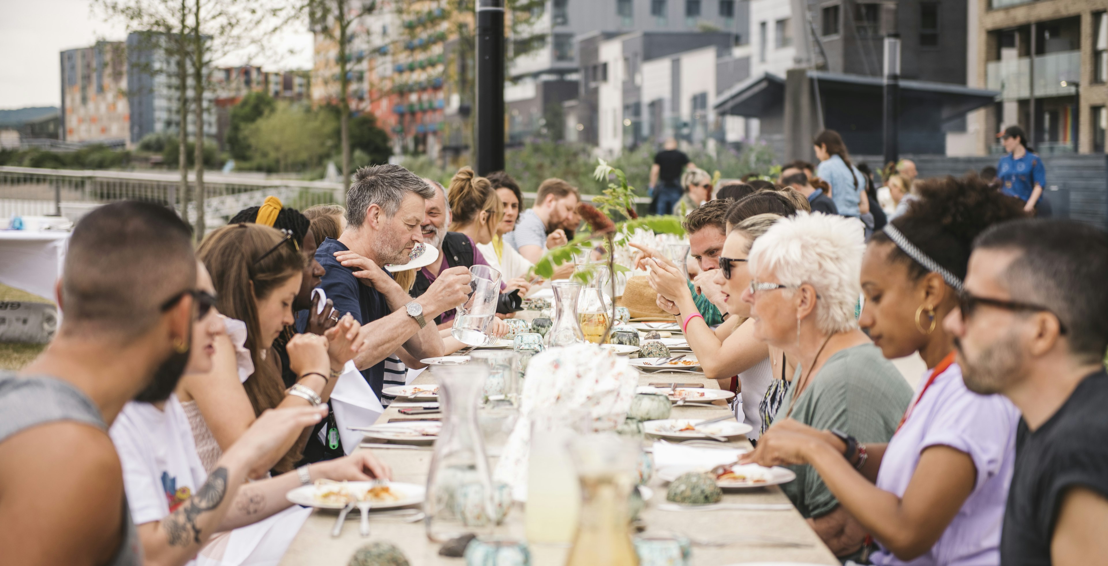 Group of people eating lunch together on long table inside Greenwich Peninsula