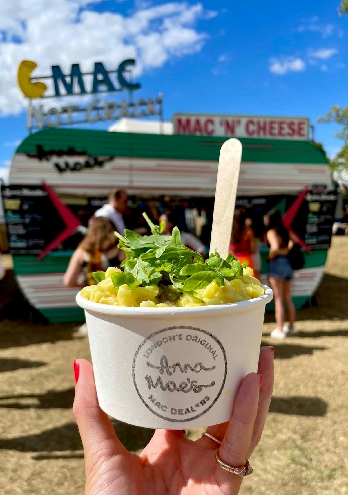 A person holds a tub of mac and cheese in front of a food truck