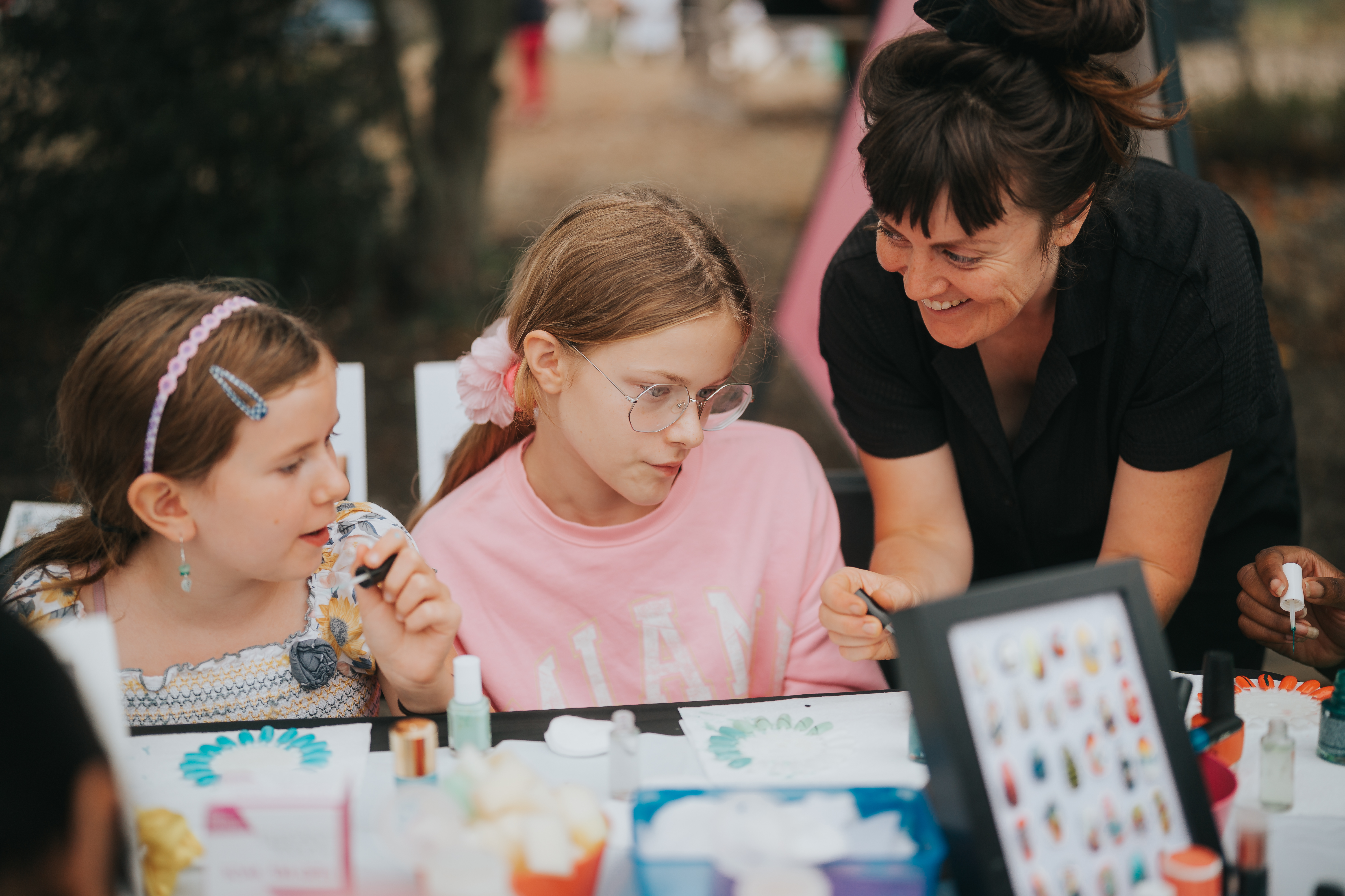 A lady shows two children some nail art