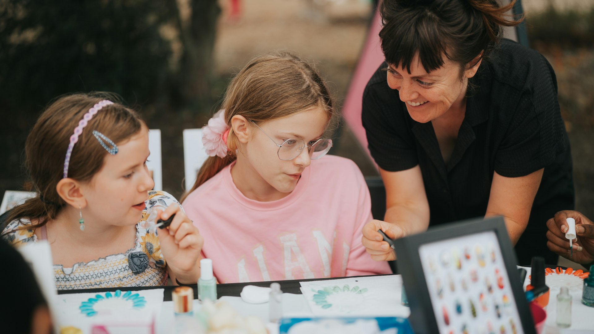 A lady shows two children some nail art