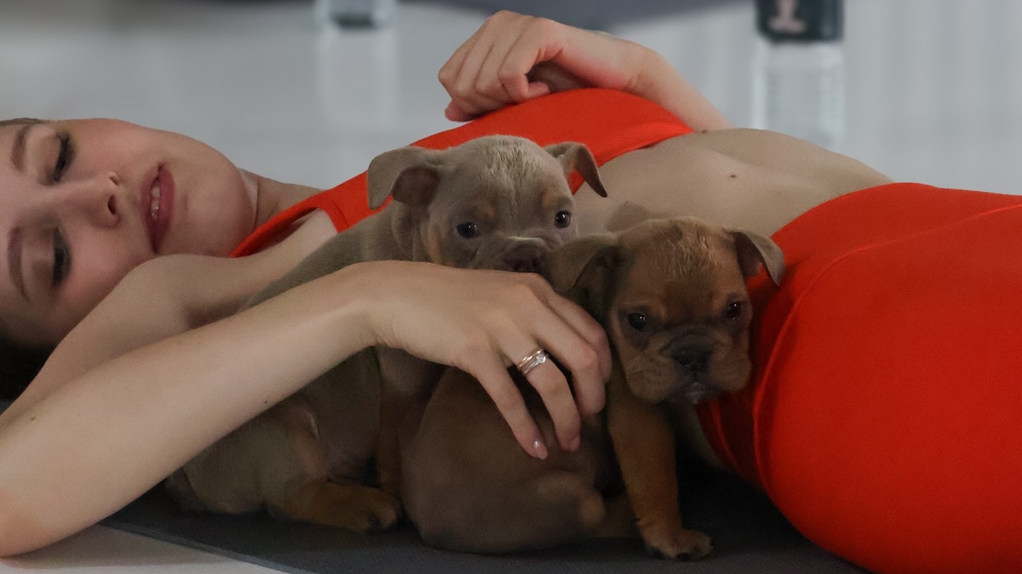 women laying down on yoga mat with two puppies cuddling her arm