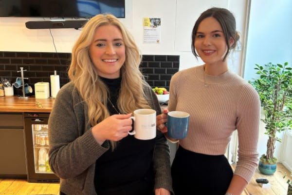 Two colleagues pictured smiling enjoying a cup of tea together.