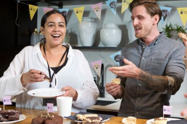 Two colleagues pictured at work enjoying cake and laughing together. 