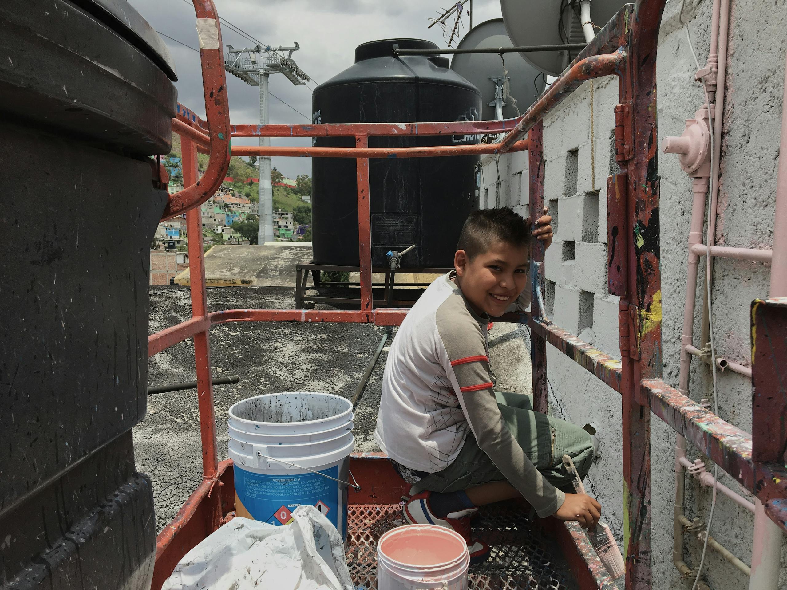 Local youth Ibrahim helps Guido with the re-painting of the building in Mexican Pink, Ecatepec, Estado de México, Mexico. July 2016 Photograph: Guido van Helten