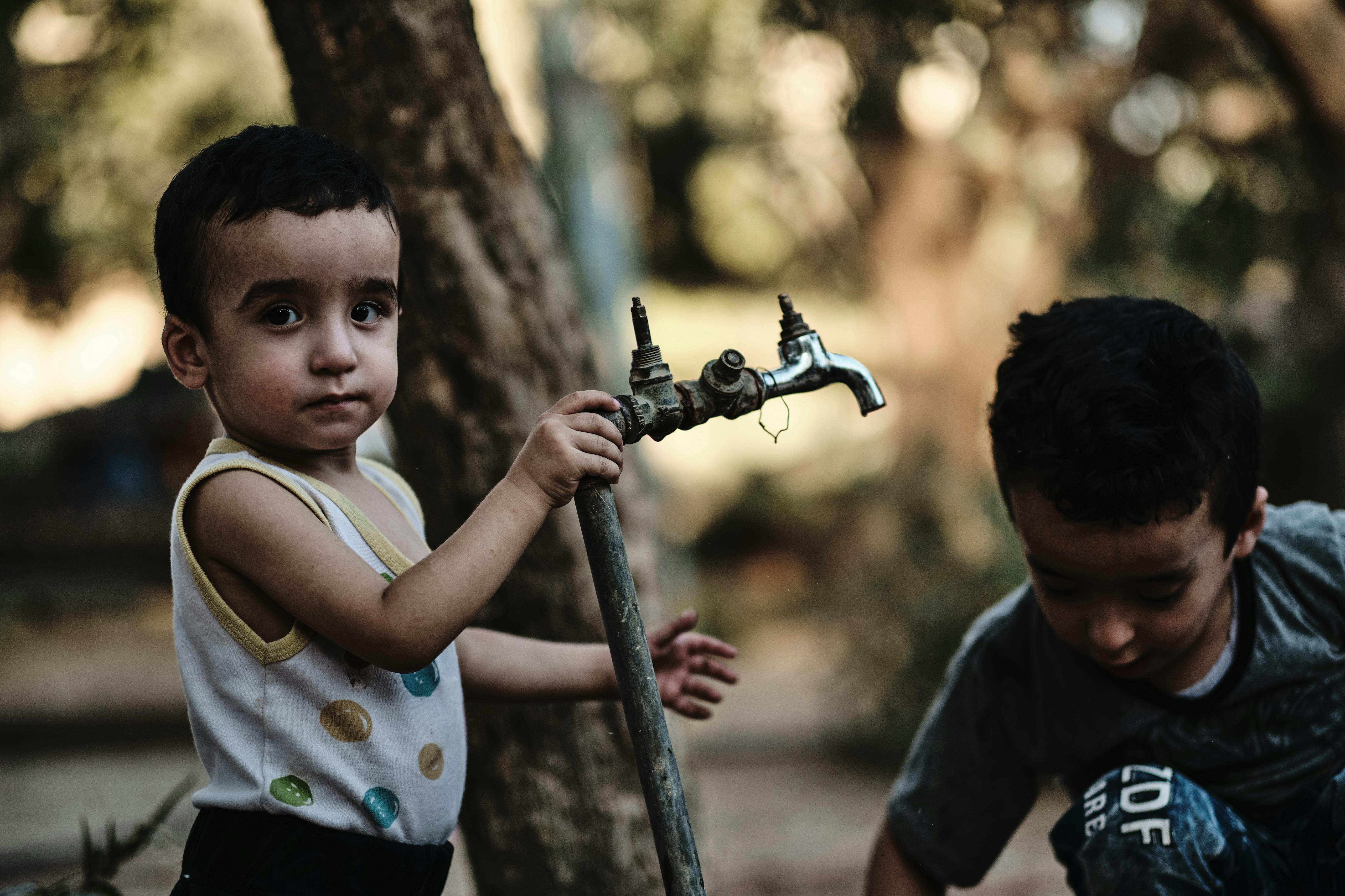 Child plays with water tap in local resident backyard, Azraq, Jordan. August 2019 Photograph: Guido van Helten