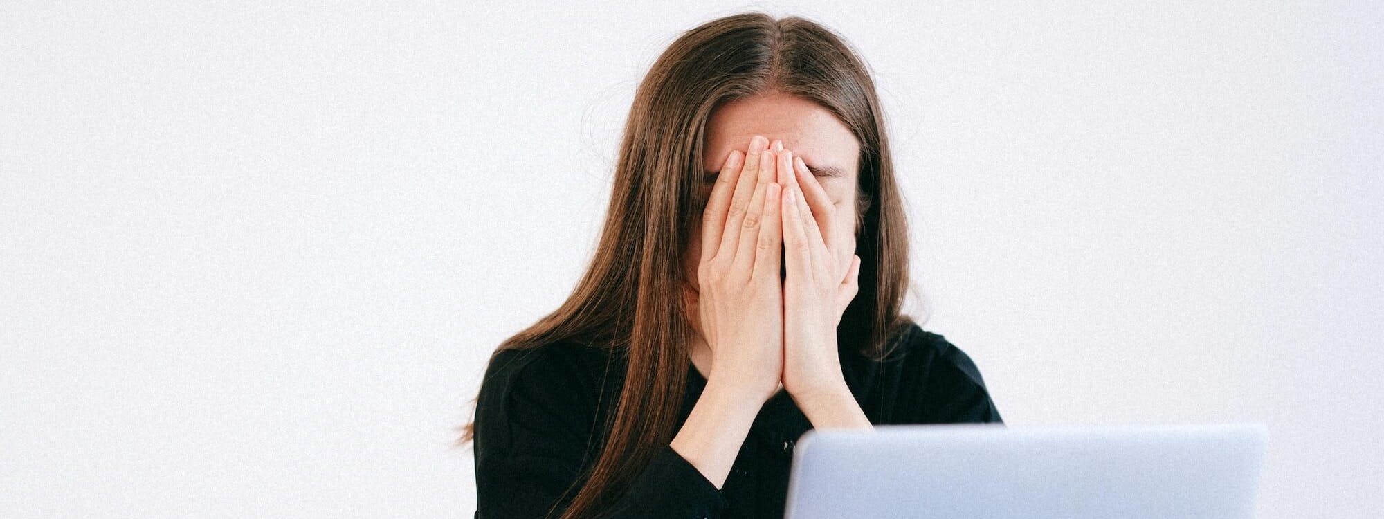 Frau sitzt vorm Laptop und hält Hände vors Gesicht