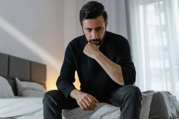 Mann sitzt nachdenklich auf seinem Bett