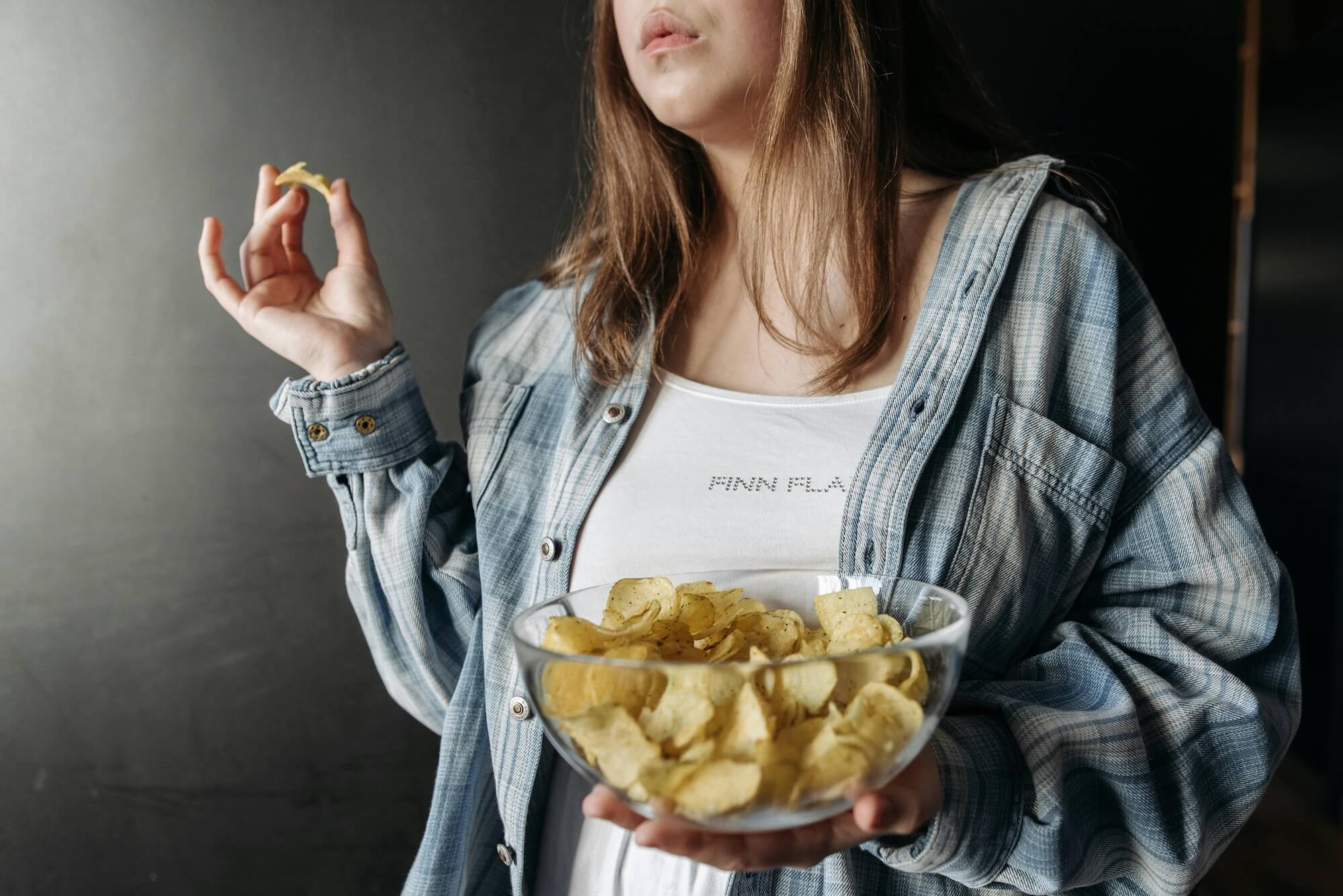 Frau isst Kartoffel Chips aus einer Glasschüssel