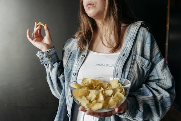 Frau isst Kartoffel Chips aus einer Glasschüssel