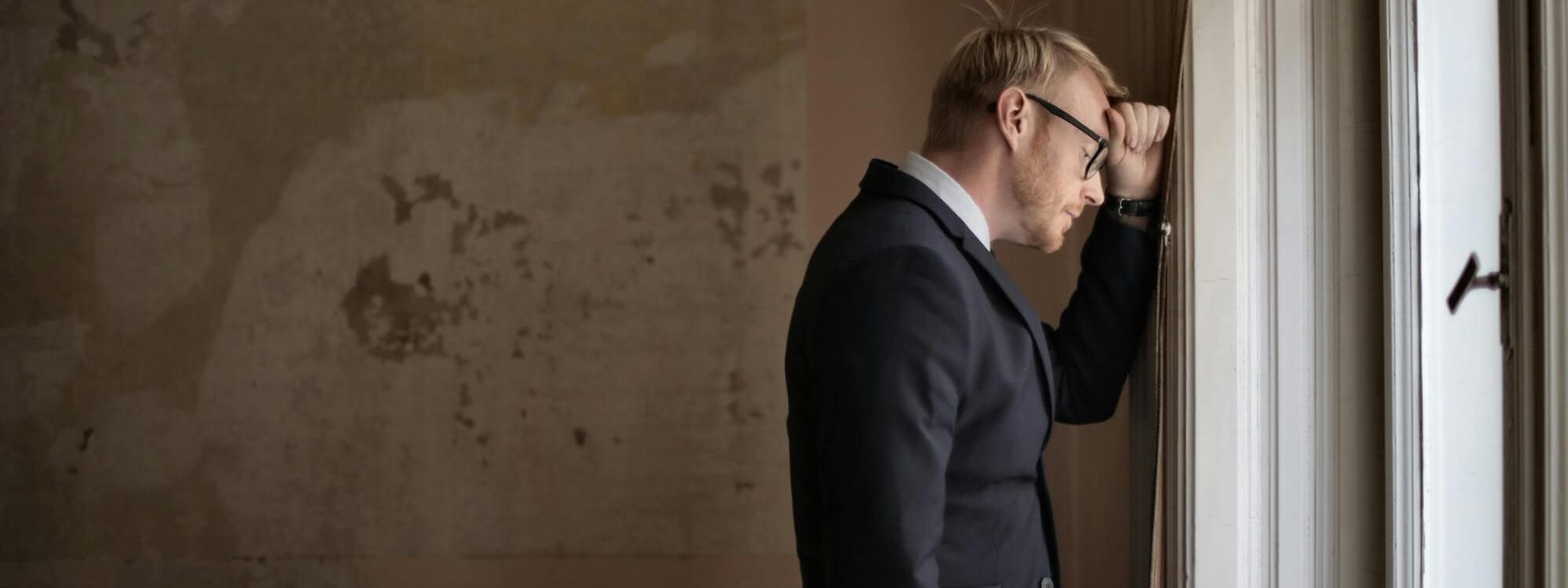 Mann steht mit Hand vorm Kopf an der Wand