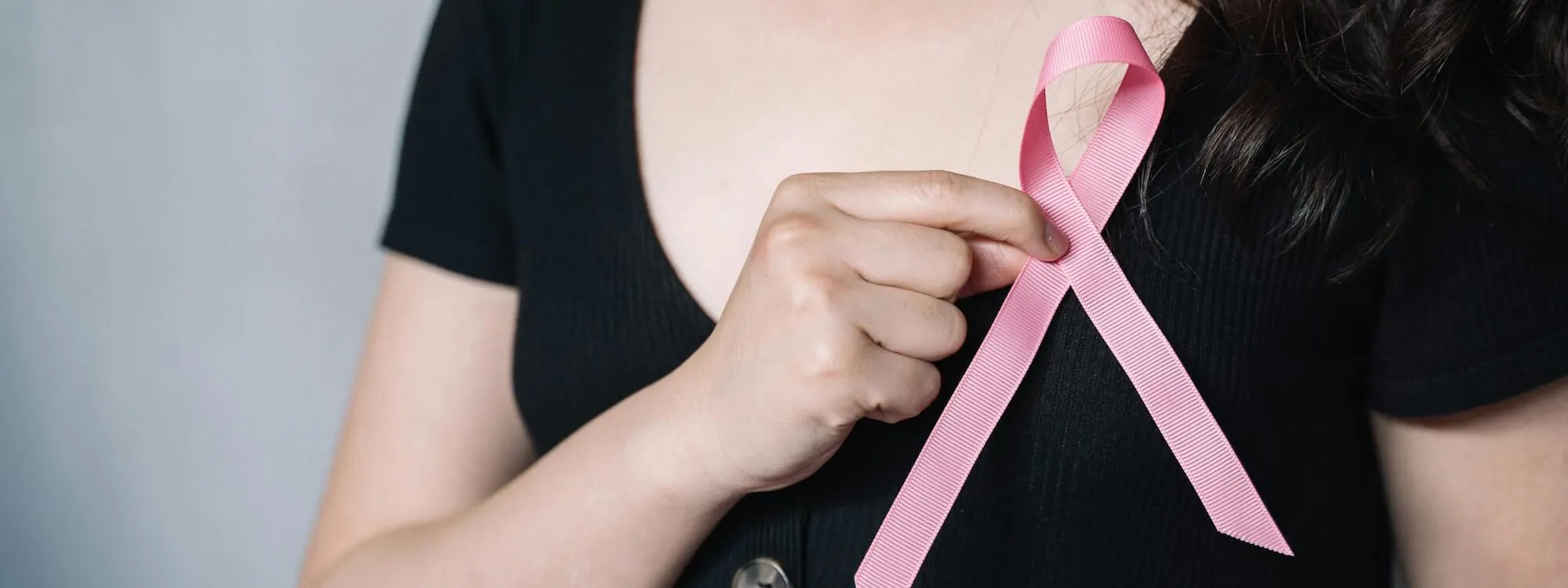 Frau hält pinke Schleife vor ihren Brustkorb