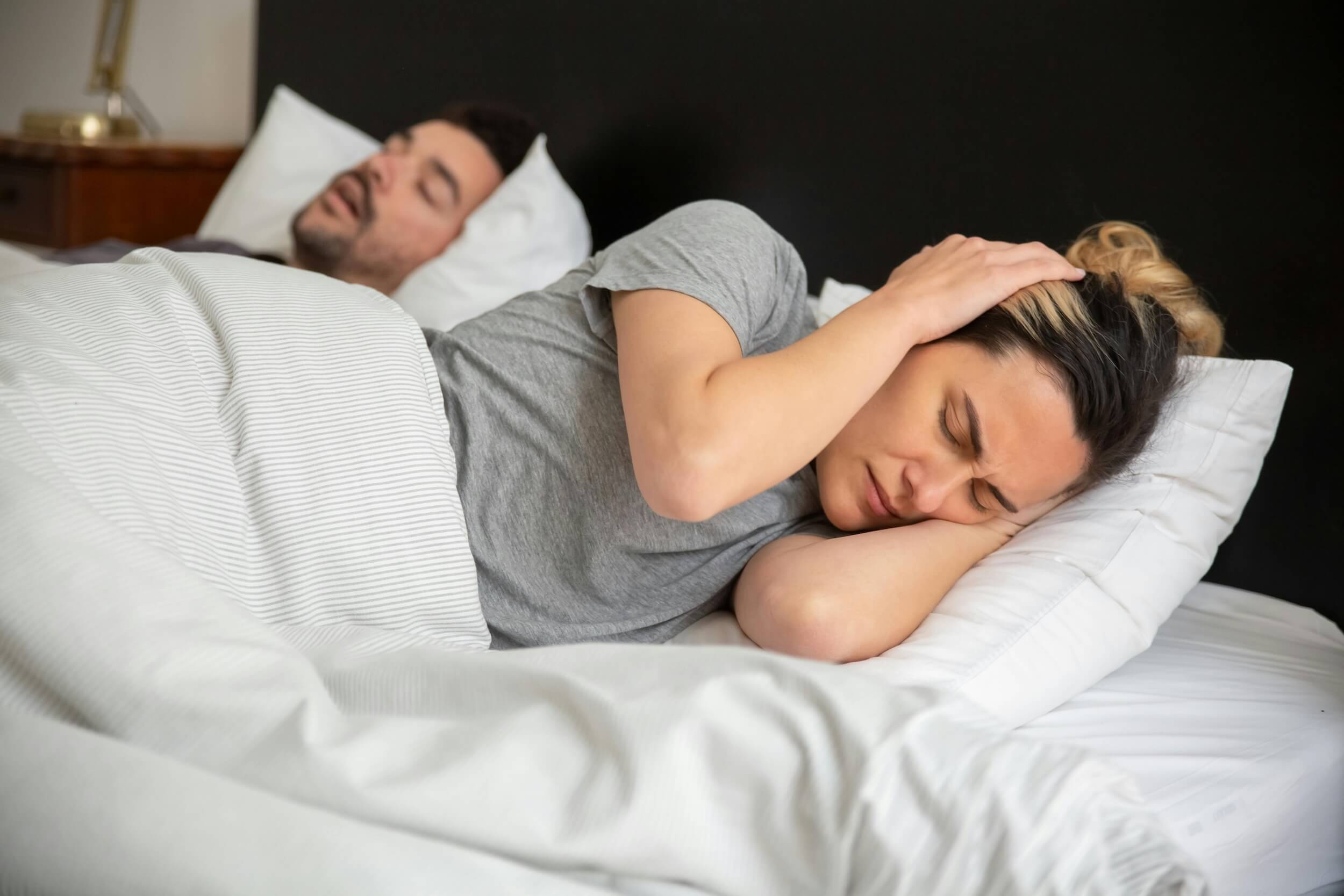 Frau liegt im Bett und hält sich die Ohren vor Schmerzen