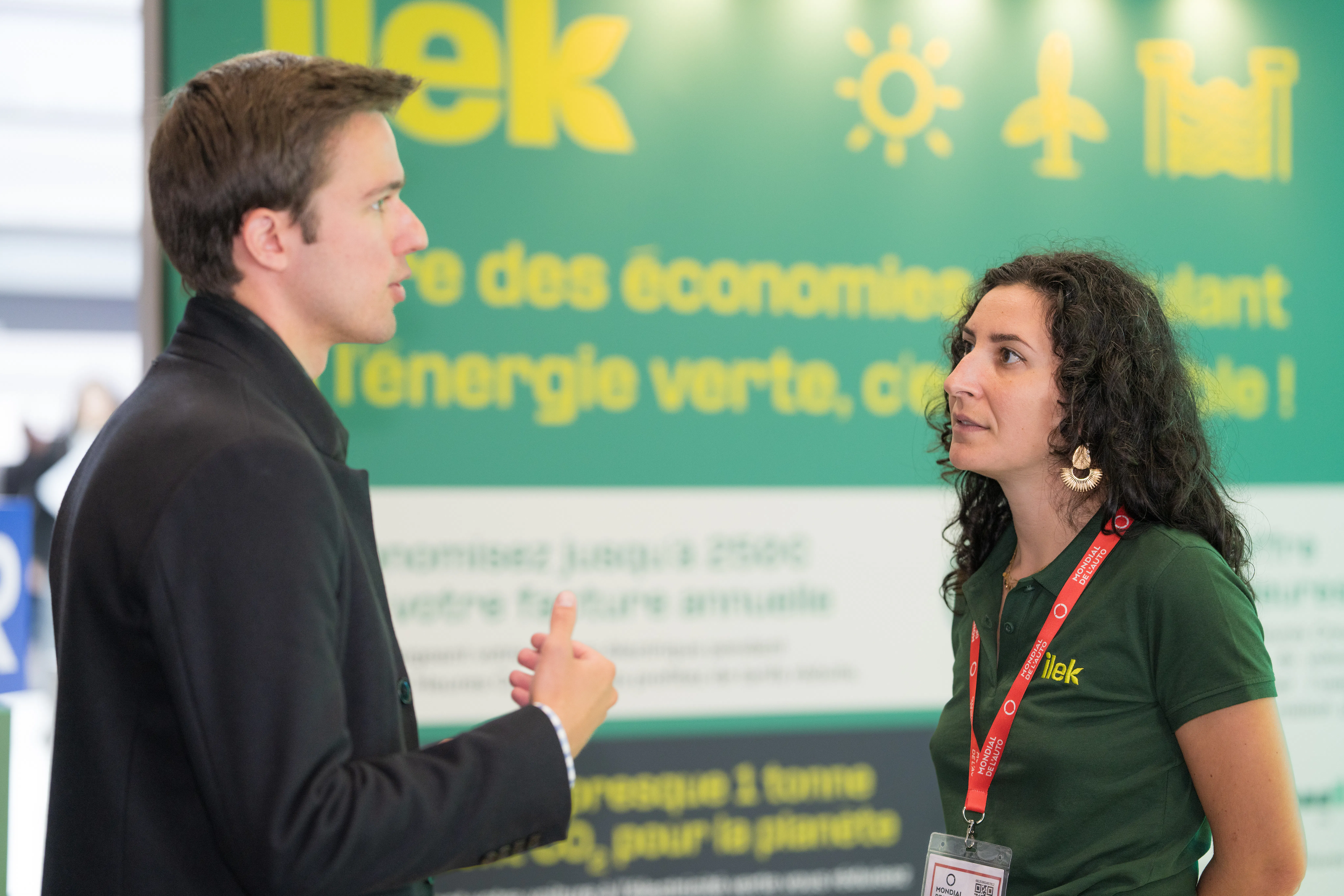 Hôtesse sur le stand Ilek expliquant l’offre de recharge de véhicules électriques 100% verte, animation et engagement client lors de l’événement.