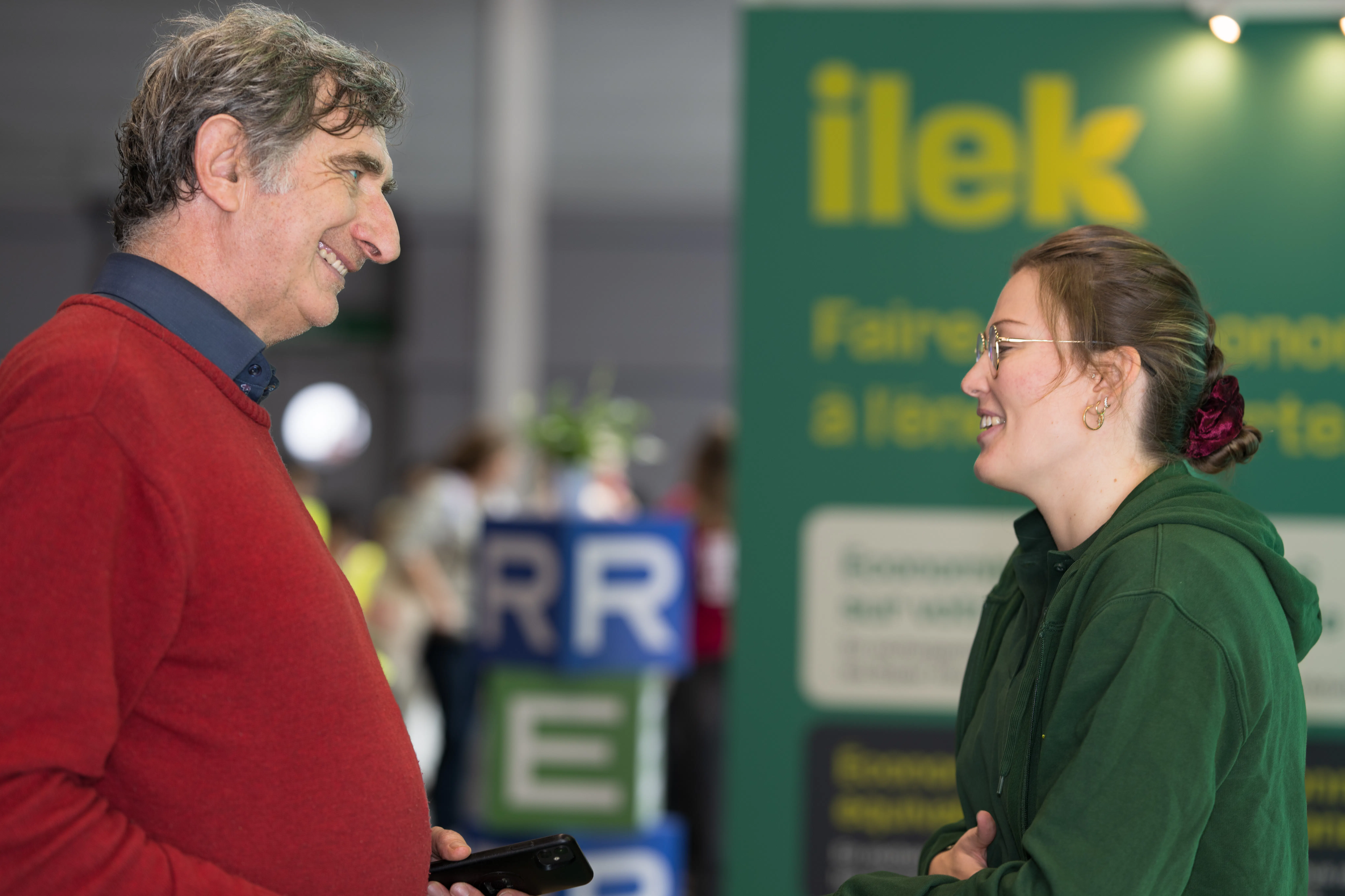 "Hôtesse sur le stand Ilek expliquant l’offre de recharge de véhicules électriques 100% verte, animation et engagement client lors de l’événement.