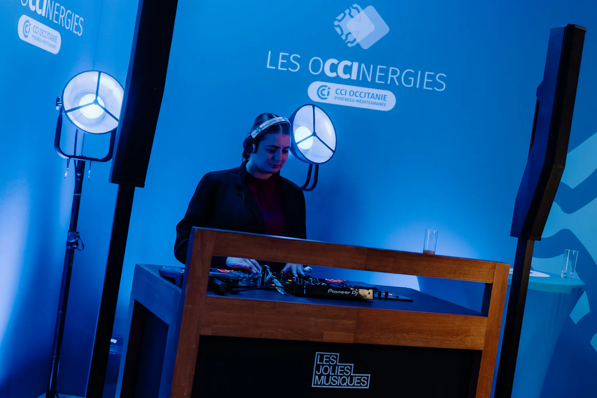 DJ présente sur scène lors d’un événement corporate, avec scénographie et branding de marque visibles.