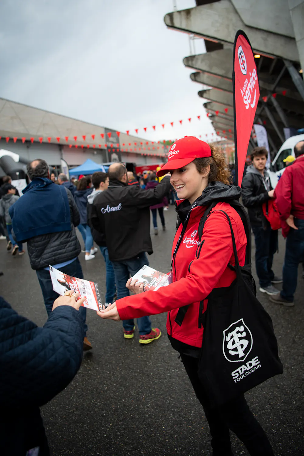 Animatrice souriante distribuant des flyers aux supporters devant le stade Toulousain