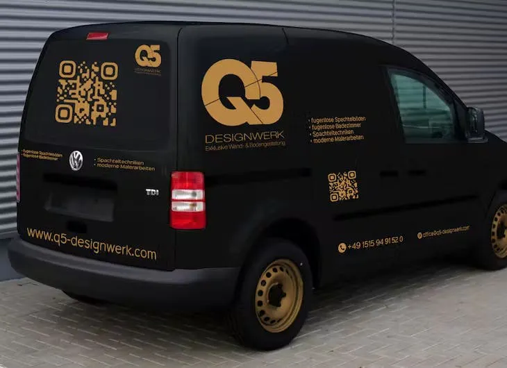 Schwarzer Transporter mit goldfarbenem Firmenlogo, QR-Codes und seitlicher Werbebeschriftung.