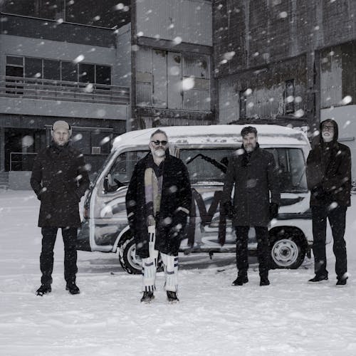 Four men in front of a van while show is falling